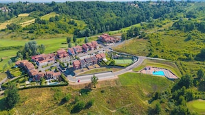 Ett flygbildsbild av ett bostadsområde med flera hus med röda tak, en swimmingpool och grönområden.