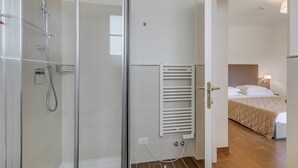 Une chambre d’hôtel dotée d’une douche à parois de verre, d’un porte-serviettes intégré et d’un lit avec une tête de lit.