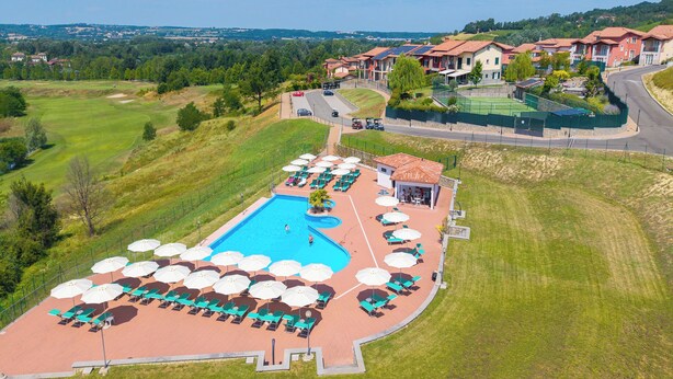 A swimming pool with sun loungers and umbrellas, surrounded by a landscaped area with a view of residential buildings. - Villa Carolina Golf View 15, Castelletto d’Orba, Italy (Castelletto d’Orba)