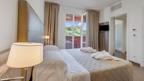 A hotel room with a bed, a lamp, a TV, and a view of the outdoors. - Villa Carolina Golf View 11, Castelletto d’Orba, Italy (Castelletto d’Orba)