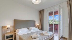 Una camera d'albergo con un letto, lampade da comodino, un comodino, vista all'esterno tramite una porta scorrevole in vetro e una luce a soffitto.
