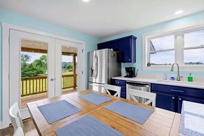 A modern kitchen with a dining area, large windows, and a view of greenery. - Lakefront Lake Anna | Hot Tub, Beach & Game Room (Orange)