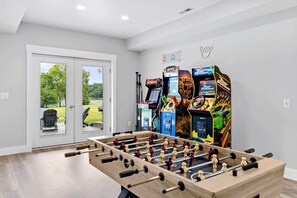 Una habitación con mesa de fútbolín, juegos de arcade y vistas a través de un ventanal.