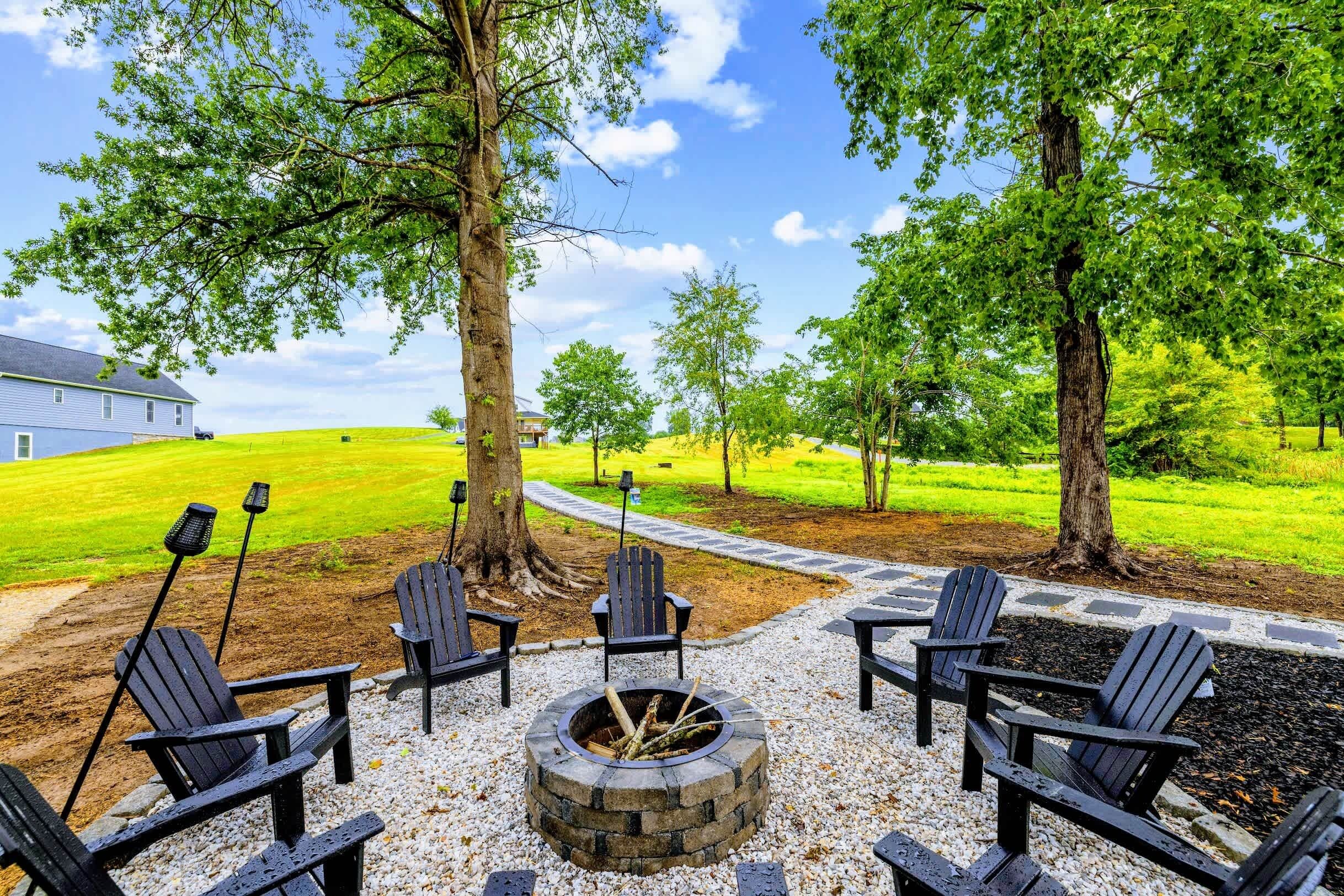 Un patio con sillas Adirondack, un hogar a leña de piedra y un sendero de grava que lleva a una casa.