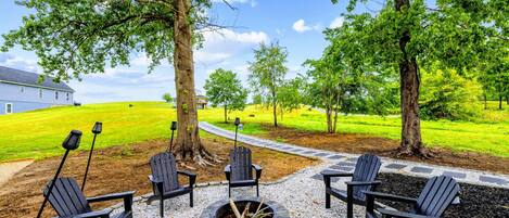 Un patio con sillas Adirondack, un hogar a leña de piedra y un sendero de grava que lleva a una casa.