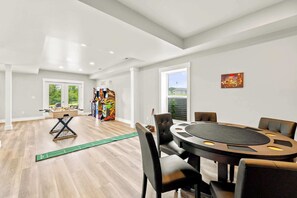 Una habitación amplia con una mesa redonda y sillas, una mesa de fútbol de mesa y una máquina recreativa de colores.