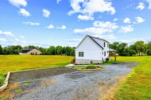 A white house with a front porch and a gravel driveway. - Lakefront Lake Anna | Hot Tub, Beach & Game Room (Orange)