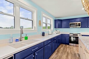 A modern kitchen with blue cabinets, a stainless steel sink, and a built-in oven. - Lakefront Lake Anna | Hot Tub, Beach & Game Room (Orange)