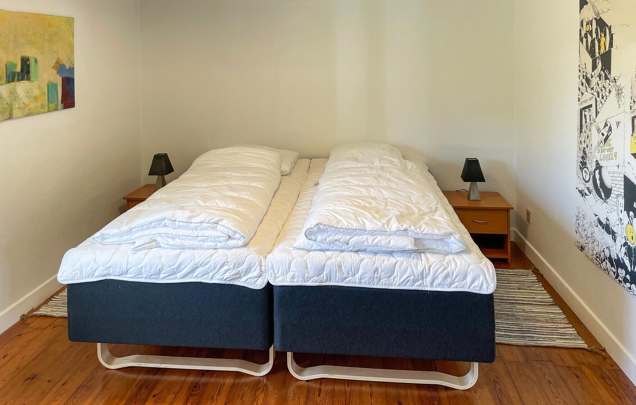 Una cama doble con ropa de cama blanca, dos mesitas de noche con lámparas y una pared con un cartel blanco y negro.