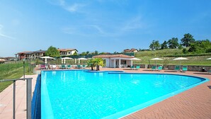 A swimming pool with a brick deck, lounge chairs, and umbrellas. - Villa Carolina Golf View 6, Castelletto d’Orba, Italy (Castelletto d’Orba)