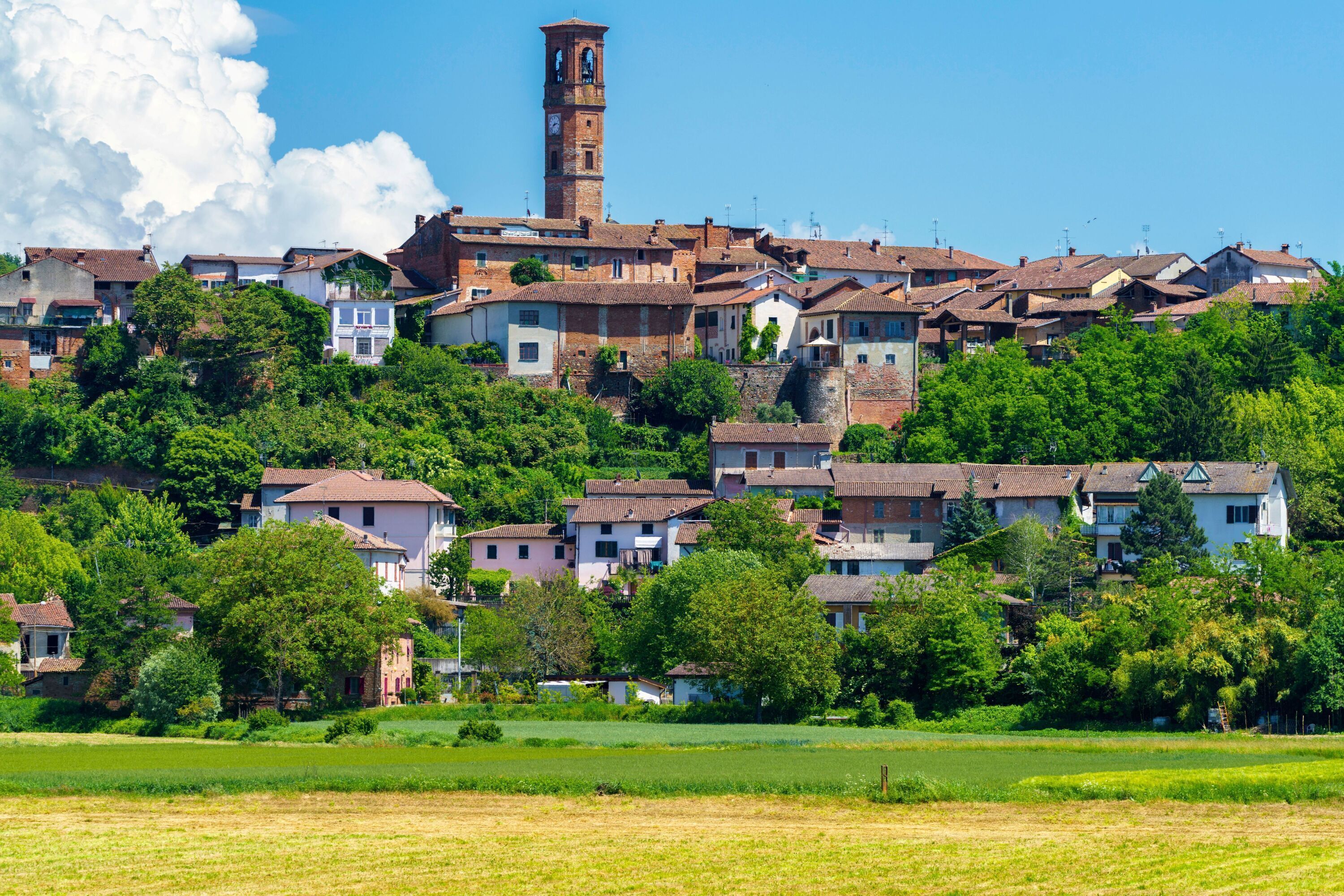 Un borgo collinare con edifici tradizionali, un'imponente torre dell'orologio e una vegetazione rigogliosa.
