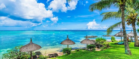 A tropical beach with clear turquoise waters, palm trees, and thatched umbrellas.