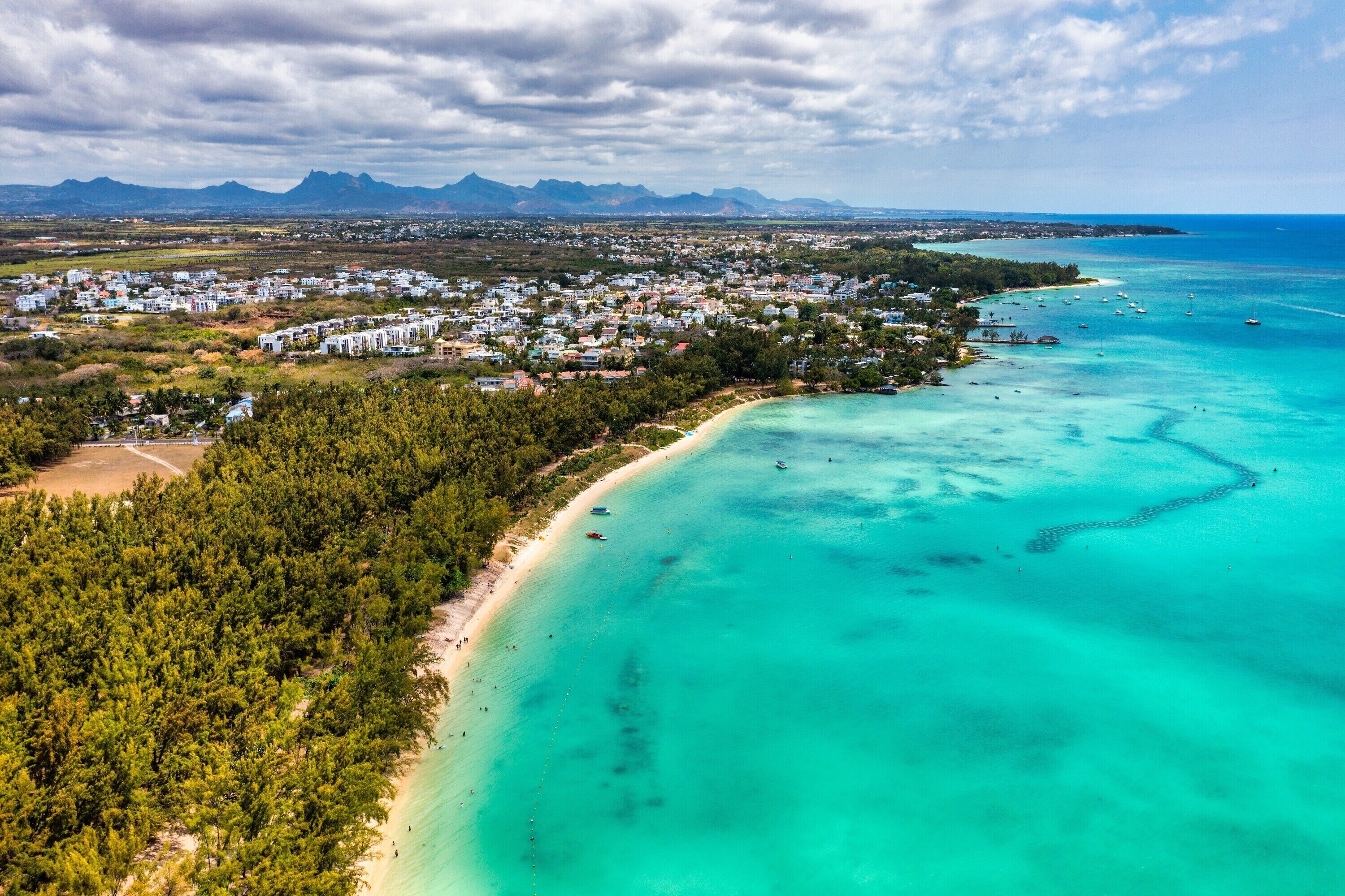 Eine Luftaufnahme einer Küstenstadt mit Strand, klarem türkisblauem Wasser und einem dichten Waldgebiet.