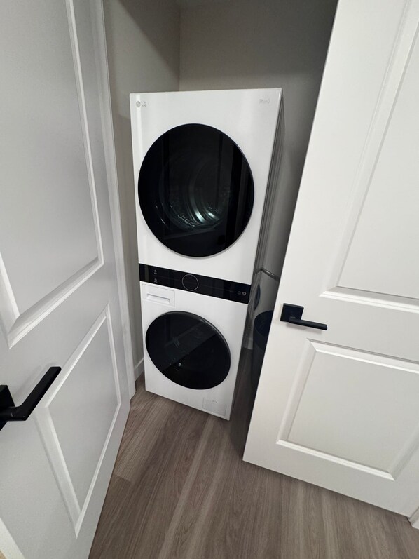 A white laundry room with two stacked washing machines, a door handle, and a wooden floor.