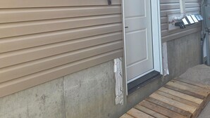 A building exterior with a metal door, a security camera, and a utility box. - Serenity Suite (Regina)
