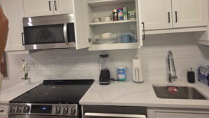 A kitchen with white cabinets, a microwave, an oven, a sink, and a countertop with various items. - Serenity Suite (Regina)