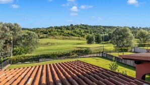 Vista di un campo da golf sotto un cielo sereno, circondato da alberi e un edificio con tetto rosso.