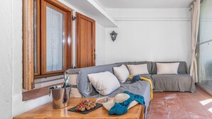 Ein gemütliches Wohnzimmer mit einem grauen Sofa, einer Holztür und einem Fliesenboden.