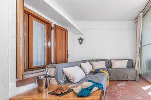 Ein gemütliches Wohnzimmer mit einem grauen Sofa, einer Holztür und einem Fliesenboden.