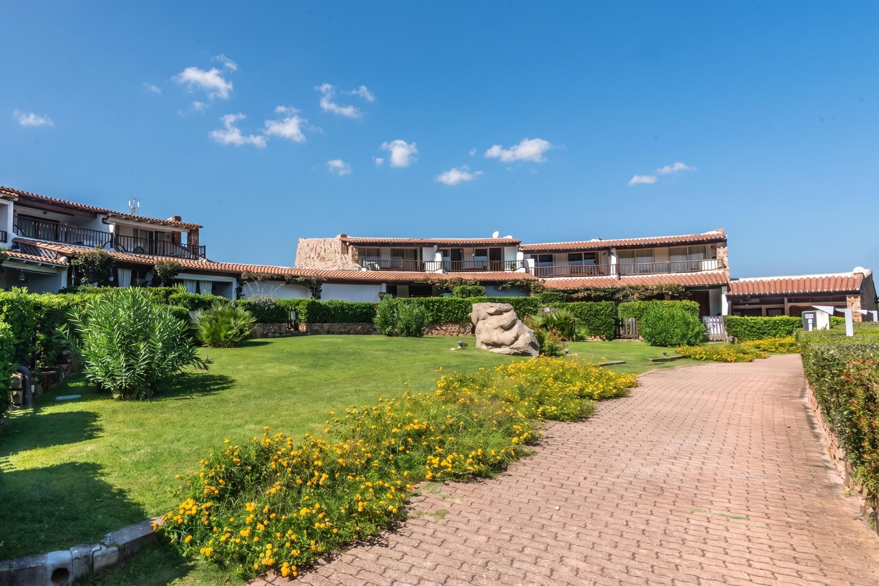 A courtyard with a paved walkway, a large rock, and a building with a tiled roof and balconies.