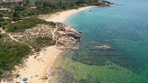 Eine Vogelperspektive auf eine Küstenlandschaft mit Sandstrand, klarem, blauem Wasser und umgebender Vegetation.