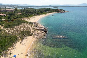 Eine Vogelperspektive auf eine Küstenlandschaft mit Sandstrand, klarem, blauem Wasser und umgebender Vegetation.