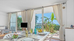 Ein Essbereich mit Tisch für zwei Personen, einem Fernseher und Blick auf den Garten durch große Fenster.