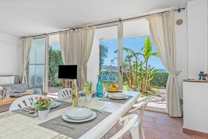 Ein Essbereich mit Tisch für zwei Personen, einem Fernseher und Blick auf den Garten durch große Fenster.