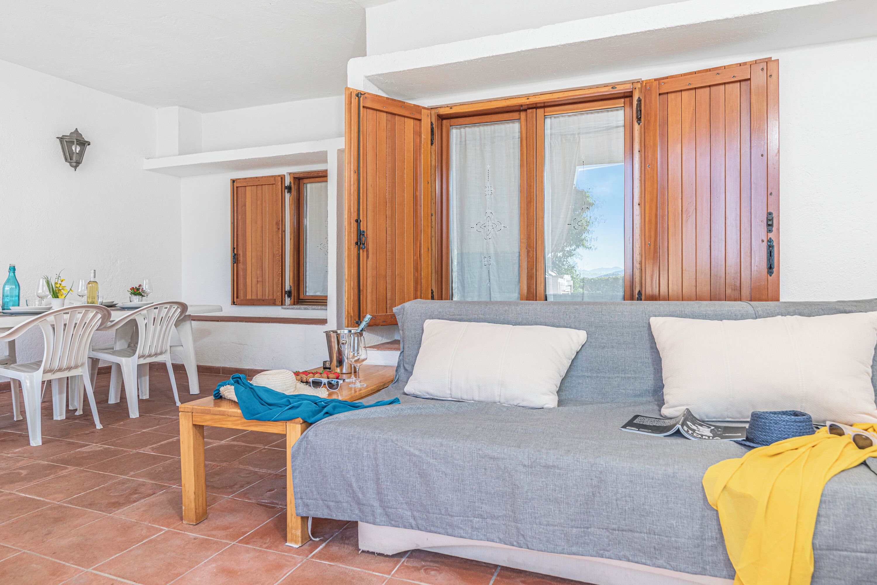 A living room with a sofa, a dining table with chairs, and wooden shutters on the windows.