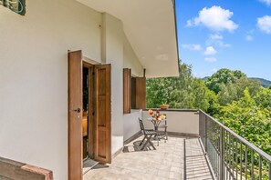 A balcony with a table and chairs, a view of greenery, and a door leading to an interior space.