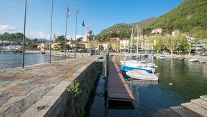 A marina with boats docked, a stone walkway, and buildings in the background.