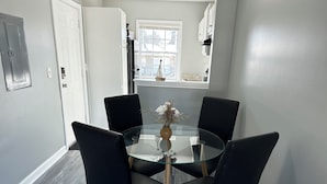 A dining area with a glass table surrounded by four black chairs, a vase with flowers, and a window with a view of the outside. - Central 1BR Birmingham Suite with Parking Near Legion Field (Birmingham)