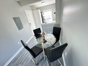 Een eethoek met een glazen tafel en vier zwarte stoelen, een witte deur, en een raam met uitzicht.