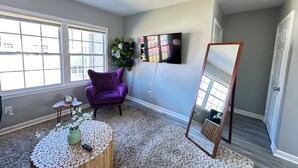 A room with a purple armchair, a round wooden coffee table with a plant, a wall-mounted TV, and a large mirror. - Central 1BR Birmingham Suite with Parking Near Legion Field (Birmingham)