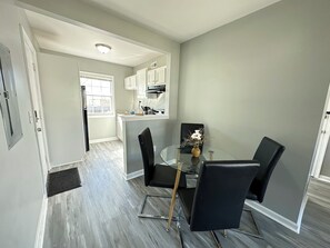 A modern kitchen with white cabinets, a dining area with a glass table and black chairs, and a grey floor. - Central 1BR Birmingham Suite with Parking Near Legion Field (Birmingham)