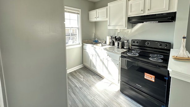 A kitchen with white cabinets, a black stove, and a window. - Central 1BR Birmingham Suite with Parking Near Legion Field (Birmingham)