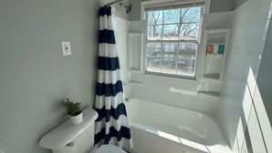 A bathroom with a shower, a toilet, a window, and a potted plant. - Central 1BR Birmingham Suite with Parking Near Legion Field (Birmingham)