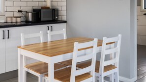 A kitchen with a wooden table and white chairs, a microwave, and a toaster on the counter. - The Vintner's Nook in Hunter Wine Country (Cessnock)