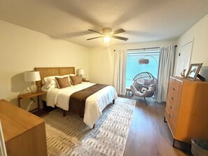 Ein Schlafzimmer mit einem Bett, Nachttischen, einem Sessel, einer Kommode und einem Deckenventilator.
