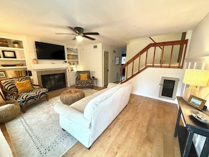 Ein Wohnzimmer mit Kamin, Fernseher, einer Couch, einem Sessel und einer Treppe.