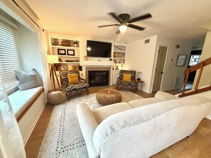 A living room with a sofa, two armchairs, a fireplace, a television, and a ceiling fan. - Southern charm awaits at Cobblestone Cottage (Wilmington)