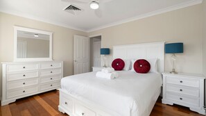Une chambre à coucher avec un grand lit, deux tables de chevet, une commode, un miroir et un ventilateur de plafond.