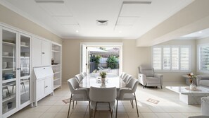 Une salle à manger moderne avec une grande table et des chaises, des meubles blancs et une vue sur un patio extérieur.