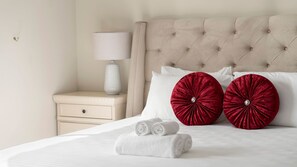 A neatly made bed with two red pillows and two rolled white towels.