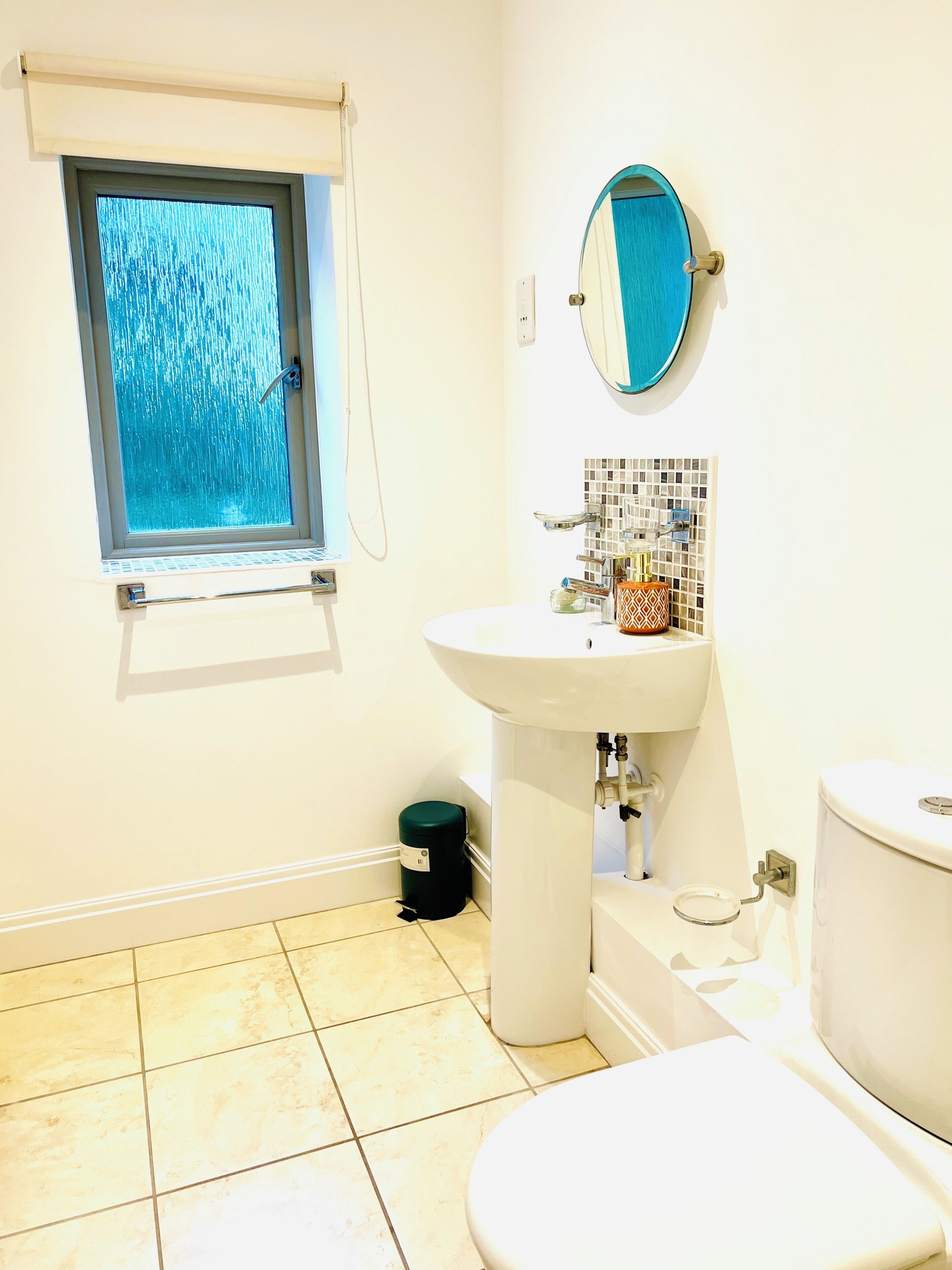A bathroom with a toilet, sink, window, and tiled floor.