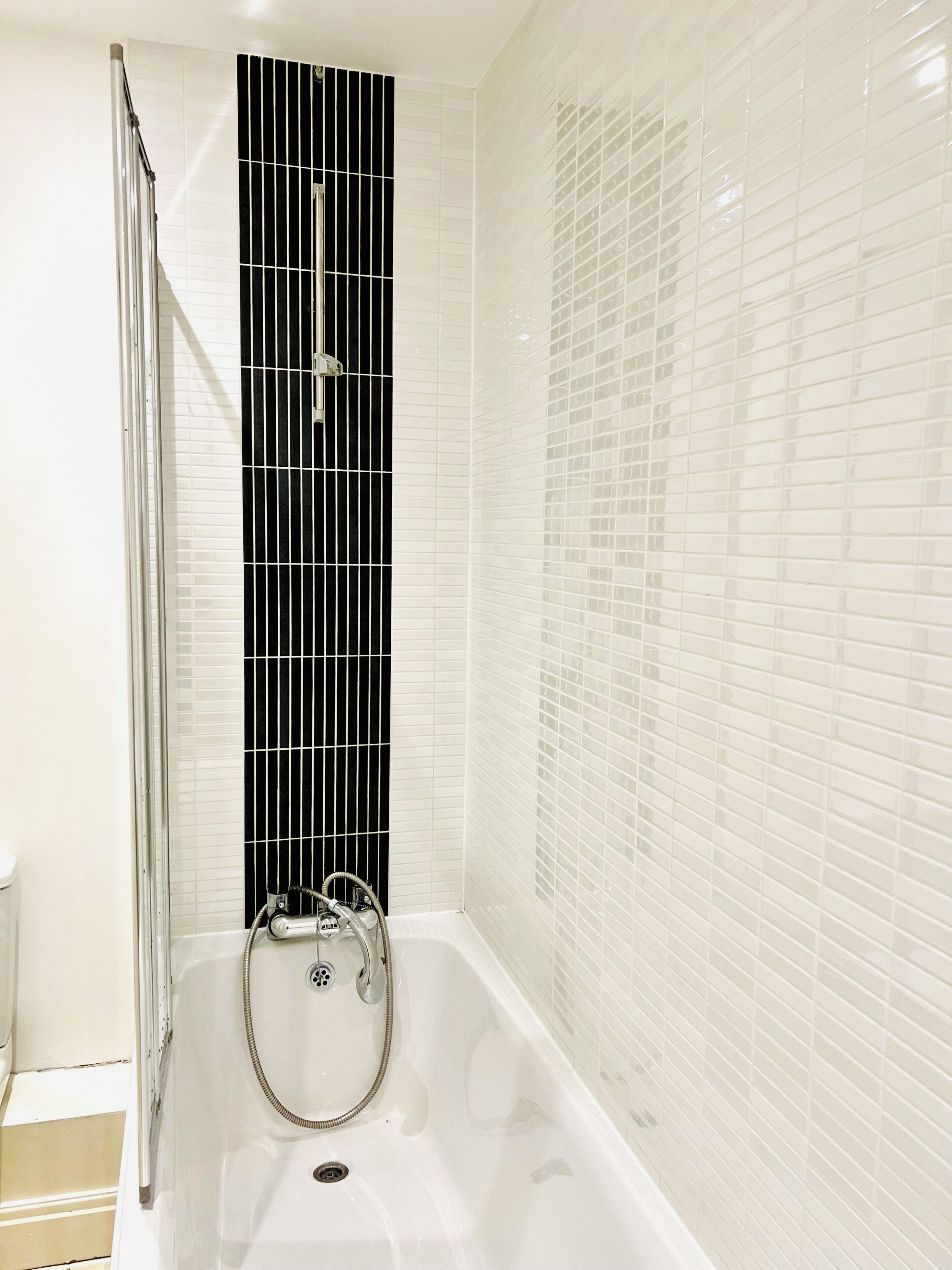 Een badkamer met een bad, een douche met een zwart paneel en witte betegelde wanden.