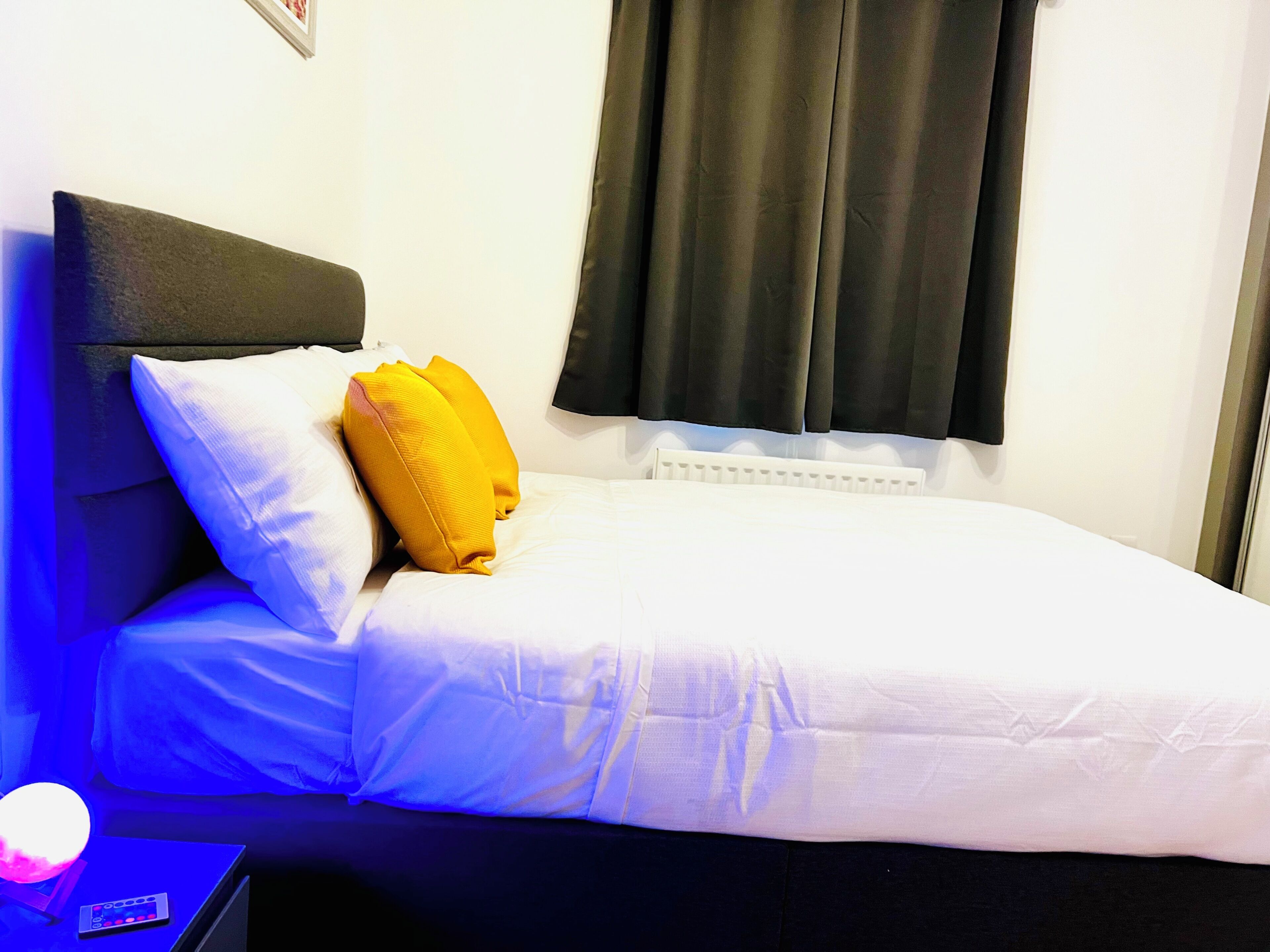 Un lit simple avec une literie blanche et une tête de lit noire, un oreiller jaune et un oreiller blanc.