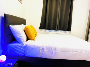 Ein Einzelbett mit weißer Bettwäsche, einem schwarzen Kopfteil, einem gelben Kissen und einem weißen Kissen.