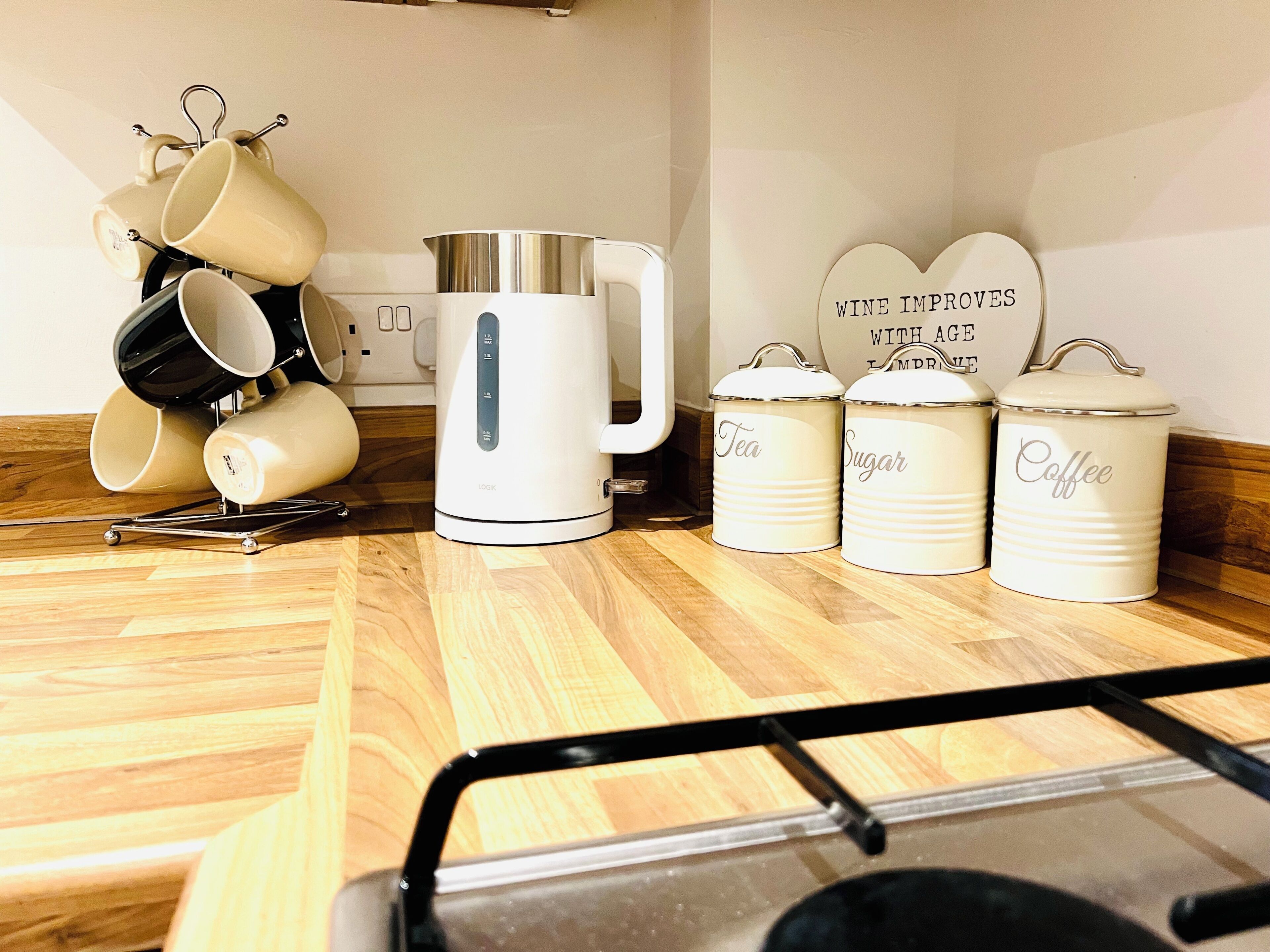 Et køkken med kaffemaskine, beholdere til te og sukker samt en hylde til kopper.
