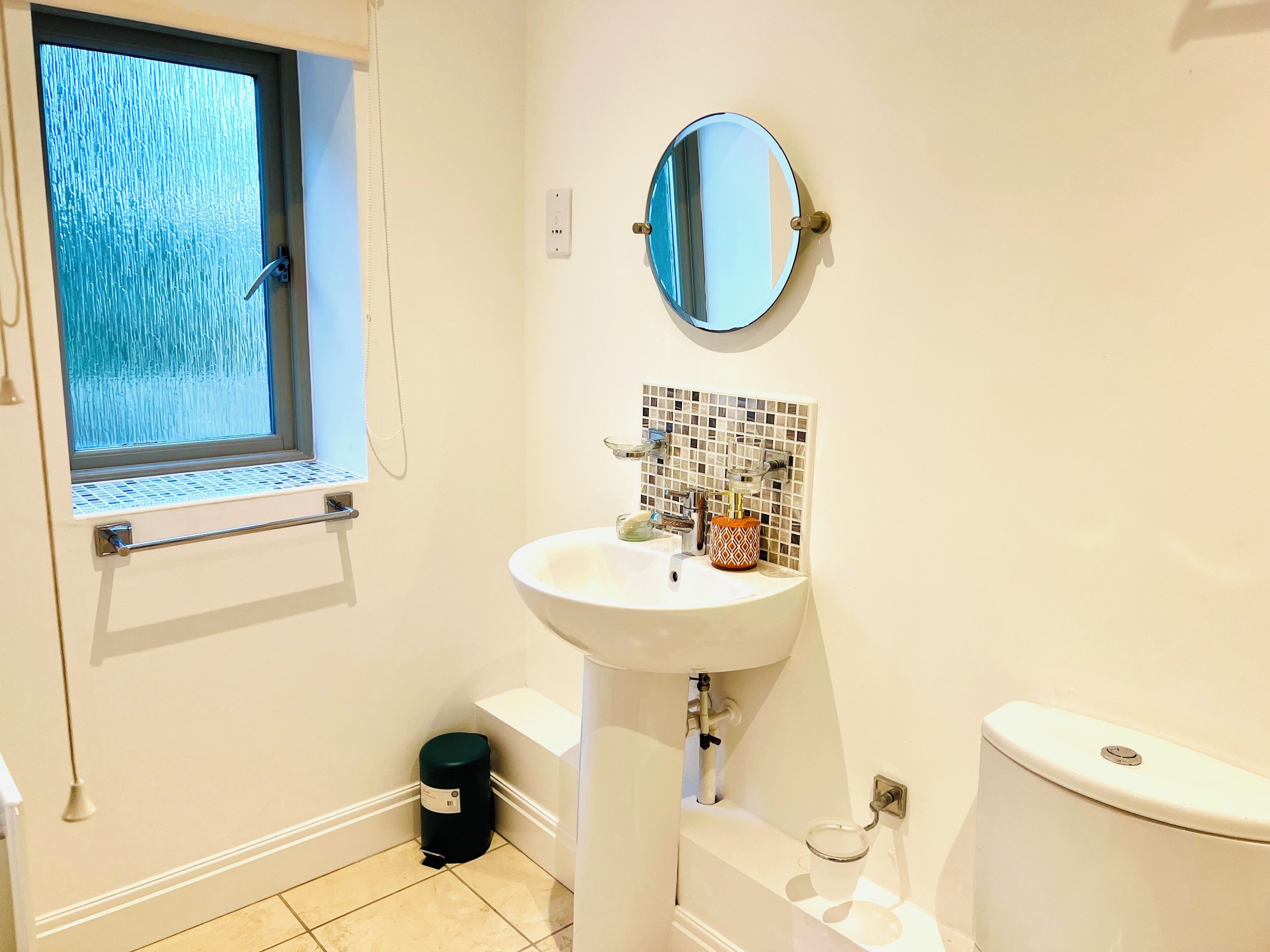 A bathroom with a window, a sink, a mirror, and a toilet.
